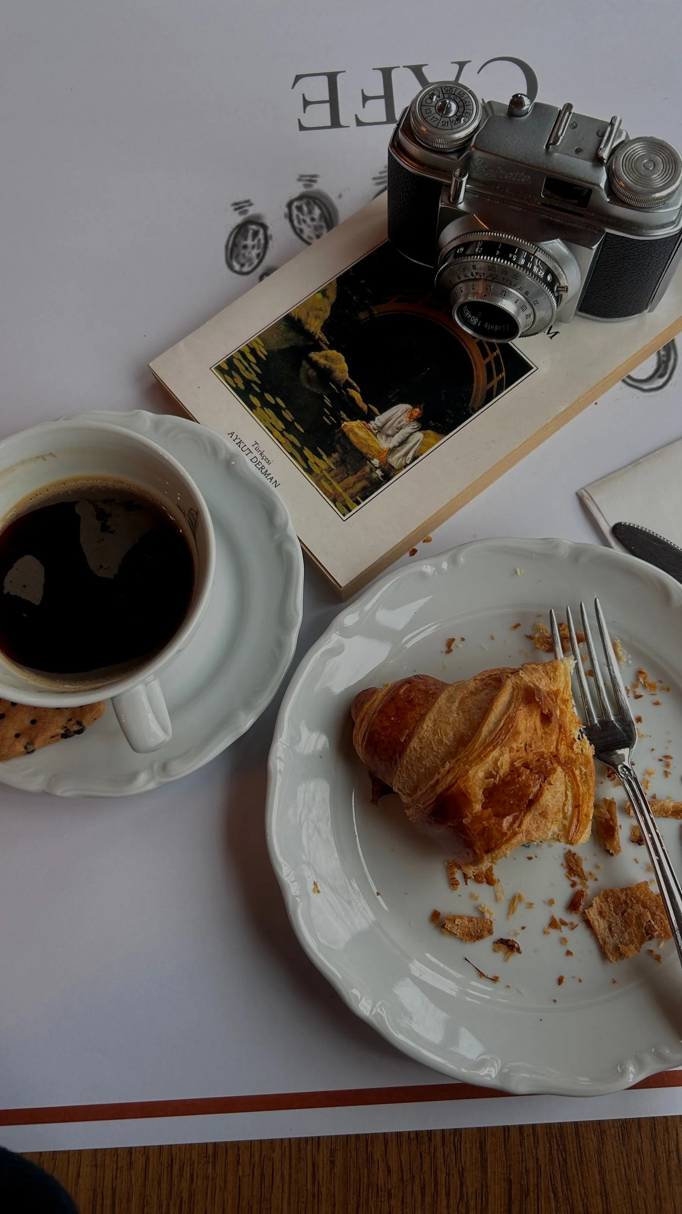 Café e croissant em mesa com livro e câmera vintage
